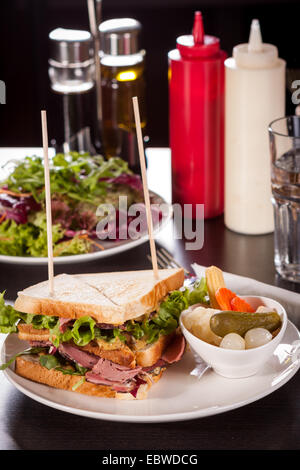 Deliziosa fette sottili di carne di manzo pastrami club sandwich con ricci fresca insalata servita con un piccolo piatto di verdure sottaceto su un Foto Stock