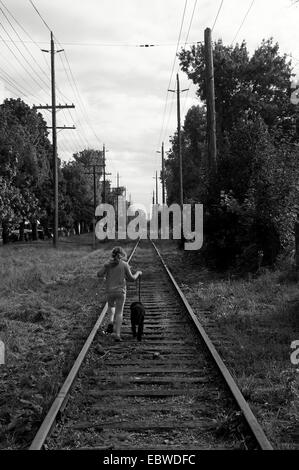 Immagine in bianco e nero di una ragazza e il suo cane che corre lungo i binari della ferrovia Foto Stock