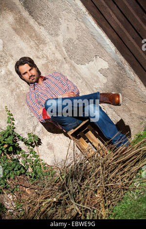 Sorridente modello maschile seduto sulla cassa di legno con le gambe incrociate Foto Stock