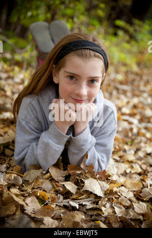 Ragazza sorridente in un ritratto verticale all'aperto in foglie di autunno Foto Stock