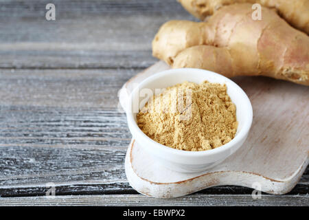 Di zenzero fresco con una piccante in polvere nella ciotola, sullo sfondo di legno Foto Stock