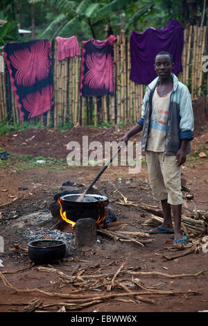 Giovane uomo cucinare un pasto sopra il fuoco sul suolo di terra del cantiere di un ristorante, Burundi, Makamba, Makamba Foto Stock