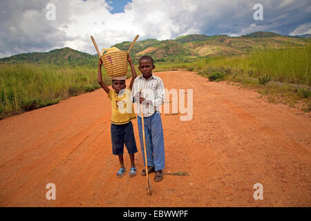 Due ragazzi con cestello e bastone in piedi sul percorso del campo, Burundi Bujumbura Mairie, Bujumbura Foto Stock