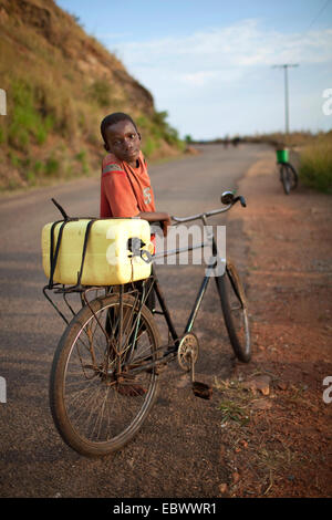 Ragazzo con una moto con un barattolo di acqua sul supporto sta prendendo una pausa al lato di una strada che porta verso l'alto, Burundi, Rumonge Rumonge, Foto Stock