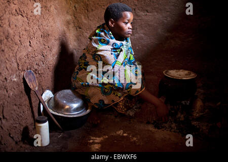 Donna in abiti tradizionali preparare un pasto sul pavimento della cucina di un umile casa di fango, Burundi, Karuzi, Buhiga Foto Stock