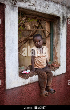 Piccolo Ragazzo seduto in una cornice per una finestra di guerra-casa danneggiata, Burundi, Karuzi, Buhiga Foto Stock