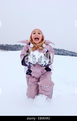 Piccola ragazza ridere mentre kneeing nella neve formando una palla di neve, Svizzera Foto Stock