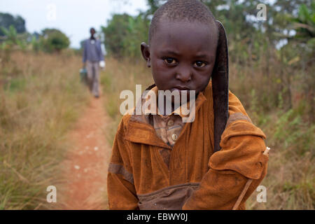 Ragazzino con machete, uomo sul percorso in background, Burundi, Karuzi, Buhiga Foto Stock