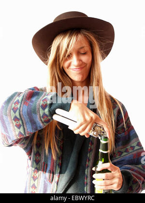 Longhaired ragazza bionda che indossa un largo-colmato hat e modellato in maniera colorata jersey è l apertura di una bottiglia con un apribottiglie Foto Stock