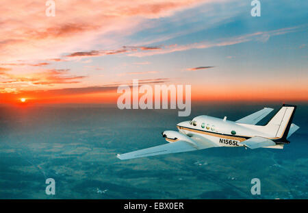Un piccolo motore twin piano di " commuters " volare verso il bellissimo tramonto arancione Foto Stock