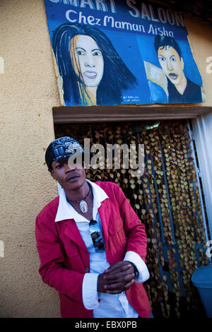 Giovane uomo di fronte a un negozio di barbiere che ha appena visitato, denominata 'Chez Maman Aisha' , il Ruanda, Nyamirambo, Kigali Foto Stock