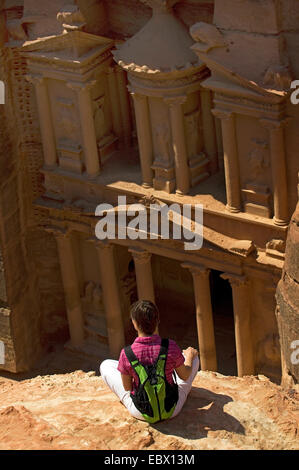 Giovani backpackers seduti su uno sperone di roccia guardando il portico del rock cut tomba denominata "tesoro" (Al Khazneh) dello storico rock cut città di Petra, Giordania Petra Foto Stock