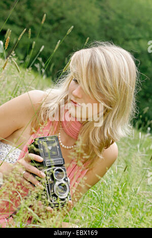 Attraente giovane donna con una vecchia foto seduta della fotocamera in un prato, Germania Foto Stock