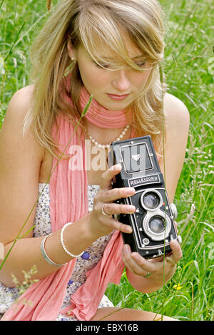 Attraente giovane donna con una vecchia foto seduta della fotocamera in un prato, Germania Foto Stock