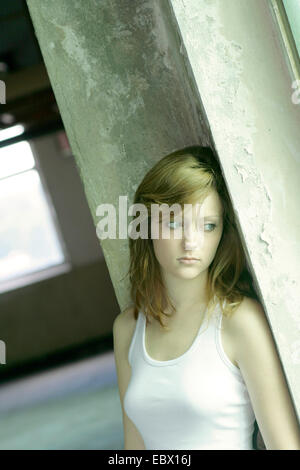 Giovane donna appoggiata contro la parete, guardando fuori della finestra perso nel pensiero, Germania Foto Stock