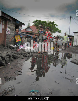 I pedoni a camminare su pietre di lava a bordo delle grandi pozzanghere dopo forti piogge durante la stagione delle piogge, Repubblica Democratica del Congo, il nord Kivu, Goma Foto Stock