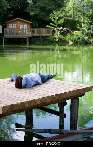 Giovane donna sdraiata su una fase di atterraggio in un stagno di relax con gli occhi chiusi Foto Stock