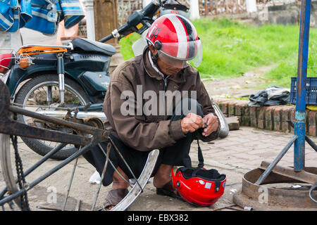 Lavoratore vietnamita di riparazione di biciclette a un mercato locale. Foto Stock