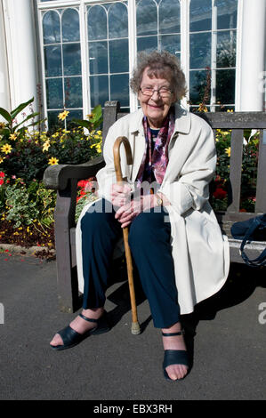 Felice vecchia donna seduta su una panca in legno a Wollaton Park godendo il sole autunnale, Regno Unito, Inghilterra, Nottingham Foto Stock