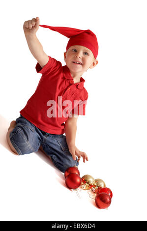 Carino il Natale di gnome. Piccolo Ragazzo in poco Santa o gnome vestiti giocando con albero di Natale giocattoli Foto Stock