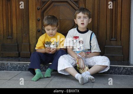 Due ragazzi seduti nella parte anteriore della porta di entrata e mangiare popcorn Foto Stock