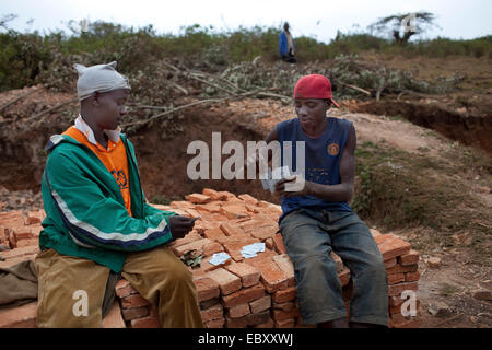 Due lavoratore seduto sulla pila di mattoni di argilla e giocare a carte, Burundi, Karuzi, Karuzi Foto Stock