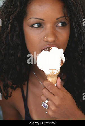 Di carnagione scura giovane donna a mangiare il gelato da un cono Foto Stock