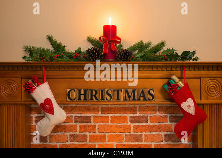 Mantelpiece con candela rossa e fresca ghirlanda fatta da holly, due calze pieno di doni appesa sopra il camino con la w Foto Stock