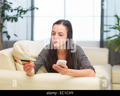 Giovane donna caucasica effettuare acquisti online tramite il telefono da casa Foto Stock