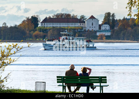 Giovane seduto su un sedile a panchina guardando un Chiemsee Pass Traghetto da, Chiemsee, Chiemgau, Alta Baviera, Deutschland, Foto Stock