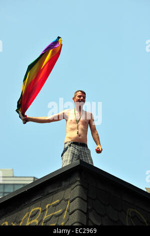 Un uomo sventola una bandiera arcobaleno su un tetto al 2014 World Pride a Toronto. Foto Stock