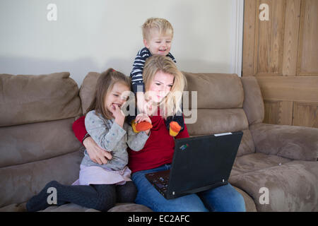 Le donne di casa utilizzando il suo computer portatile con bambini sul divano Foto Stock