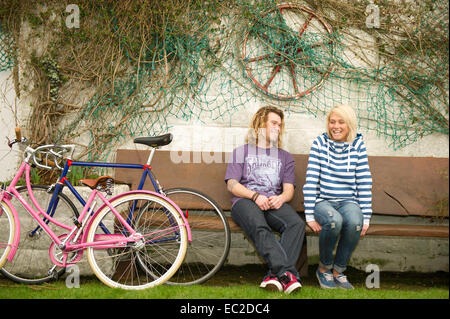 Una coppia giovane seduto su una panchina a ridere Foto Stock