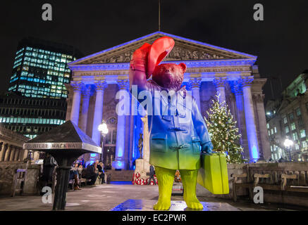 Statua colorata di Paddington Bear promuovere il film al di fuori del illuminato blu Royal Exchange, City of London, in aiuto del NSPCC, di notte Foto Stock