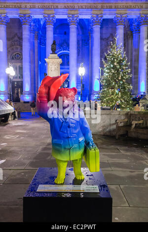 Statua colorata di Paddington Bear promuovere il film al di fuori del illuminato blu Royal Exchange, City of London, in aiuto del NSPCC, di notte Foto Stock