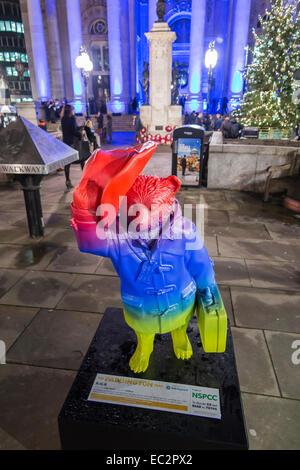 Statua colorata di Paddington Bear promuovere il film al di fuori del illuminato blu Royal Exchange, City of London, in aiuto del NSPCC, di notte Foto Stock