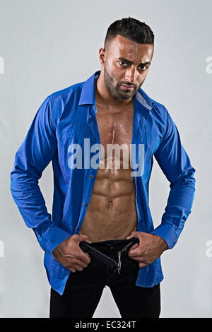 Montare giovane maschio indiano con la maglietta blu rimosse con le mani nei pantaloni neri Foto Stock
