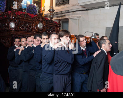 Processione del Martedì Santo la notte della settimana di Pasqua in Algeciras. I membri di fraternità indossando un pesante la figura di Gesù Foto Stock