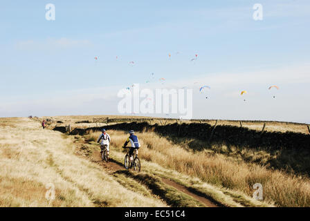Gli amanti della mountain bike in direzione est lungo Rushup Edge, scuro, di picco Peak National Park, Derbyshire, Regno Unito. I parapendii sopra. Foto Stock