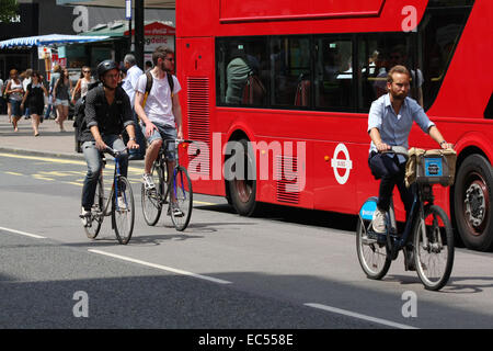 Tre i ciclisti il sorpasso di un rosso London bus ad una fermata di autobus di Oxford Street, Londra Foto Stock