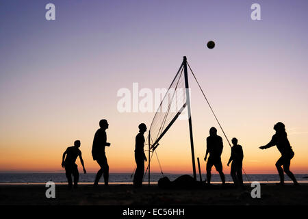 Sagome di un gruppo di giovani persone a giocare a beach volley sulla spiaggia in Bretagna, Francia Foto Stock