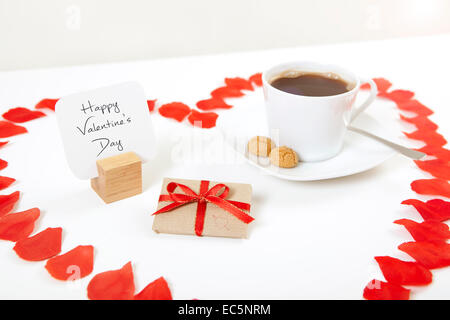 Tavolo per la colazione per il giorno di San Valentino con il dono e il caffè incorniciato con un cuore di petali di rosa Foto Stock