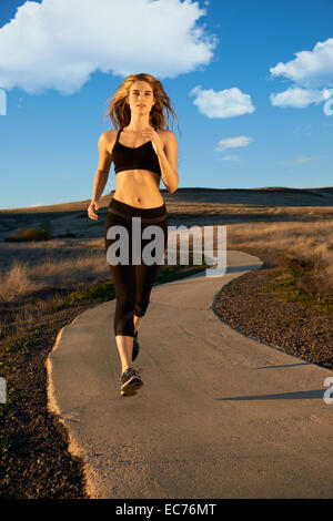 Una giovane donna in nero active wear jogging su un esterno di corsa su una caduta nel pomeriggio. Foto Stock