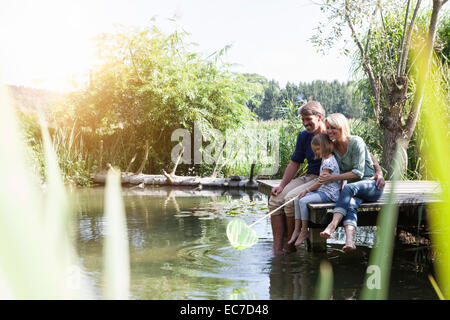 La famiglia felice seduta con dip net sul pontile di un lago Foto Stock