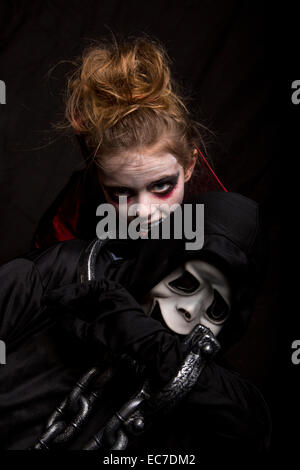 Ragazza masquarade come vampire mordere ragazzo che indossa la maschera di Scream Foto Stock