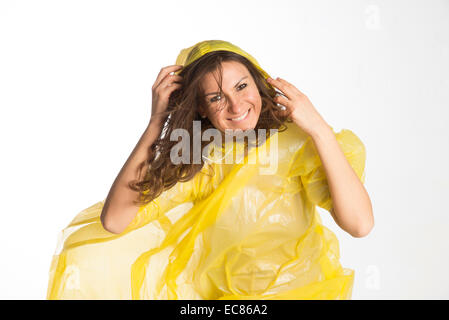 Donna che indossa un giallo poncho di plastica e trattenere il cofano in umidità condizioni ventose Foto Stock