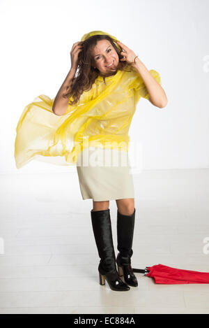 Donna che indossa un giallo poncho di plastica e trattenere il cofano in umidità condizioni ventose Foto Stock