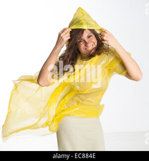 Donna che indossa un giallo poncho di plastica e trattenere il cofano in umidità condizioni ventose Foto Stock