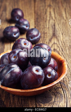 Prugne fresche nella ciotola sul vecchio tavolo in legno Foto Stock