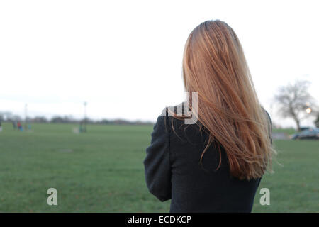 Vista posteriore del colpo di una giovane donna in piedi cercando la distanza in un parco. Foto Stock